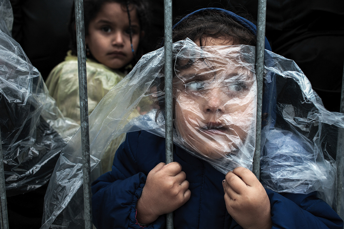 PRESEVO, SERBIA - OCTOBER 7, 2015: A child refugee is covered with raincoat while she waits in line to get registered in Presevo refugee registration camp. Most of the refugees who crossed Serbia try to continue their route towards Hungary, Croatia, Slovenia and other countries of the European Union.